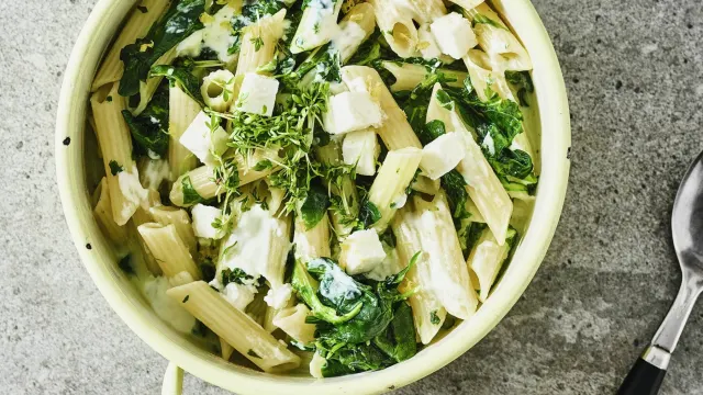 Cremige One-Pot-Nudeln mit Blattspinat, halbierten Kirschtomaten und geriebenem Parmesan in einem tiefen Teller