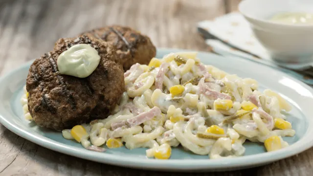Zwei gebratene Buletten mit cremigem Nudelsalat aus Makkaroni, Mais, Schinken und Gewürzgurken