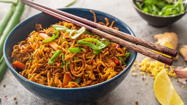 Gebratene asiatische Mie-Nudeln mit Paprika, Brokkoli, Möhren, Pilzen und Frühlingszwiebeln in einer Schale