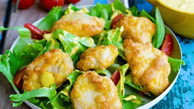 Knusprige Chicken Nuggets auf gemischtem Salat mit Gurke, Tomaten, Mais und roten Zwiebeln