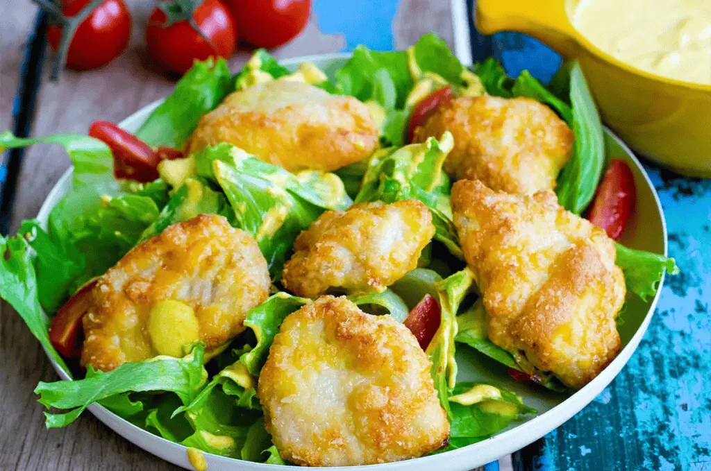 Knusprige Chicken Nuggets auf gemischtem Salat mit Gurke, Tomaten, Mais und roten Zwiebeln