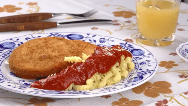 Panierte goldbraune Jagdwurstscheiben mit Spirelli und roter Tomatensoße auf einem Teller