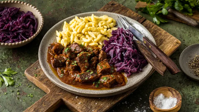 Dunkles Gulasch mit zarten Fleischstücken und in Butter geschwenkten Spätzle auf einem Teller