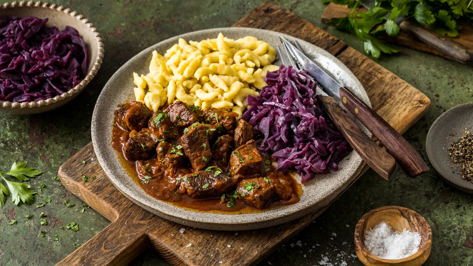 Dunkles Gulasch mit zarten Fleischstücken und in Butter geschwenkten Spätzle auf einem Teller