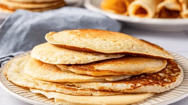 Stapel goldbrauner dünner Pfannkuchen auf einem Teller mit Puderzucker und frischen Beeren