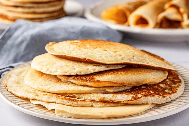 Stack of thin golden-brown German pancakes on a plate with powdered sugar and fresh berries