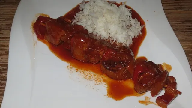 Schaschlikspieße mit Schweinefleisch, Paprika, Zwiebeln und Speck in Tomatensoße neben Basmatireis und gemischtem Salat