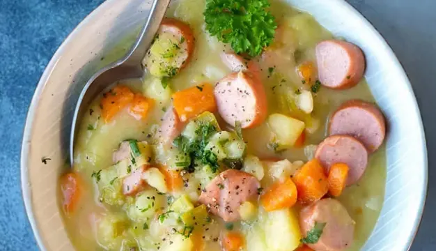 Kartoffelsuppe mit Würstchenscheiben, Kartoffel- und Möhrenstücken und grünen Kräutern in einer Schale.